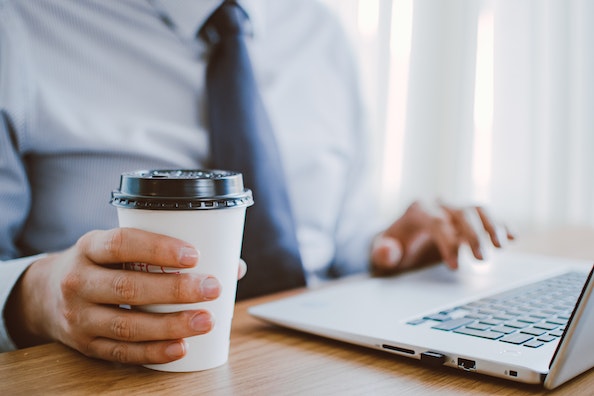 Person holding a coffee cup in one hand and typing on their laptop with the other